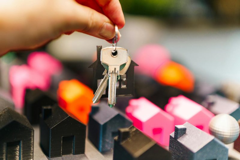 Colorful miniature houses and a hand holding keys representing real estate decisions